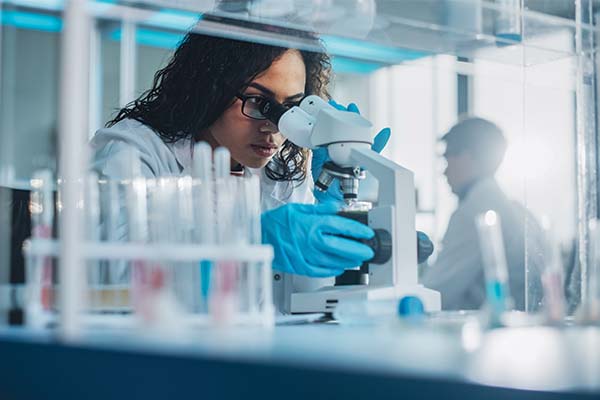 Woman looking through microscope in a lab with test tubes