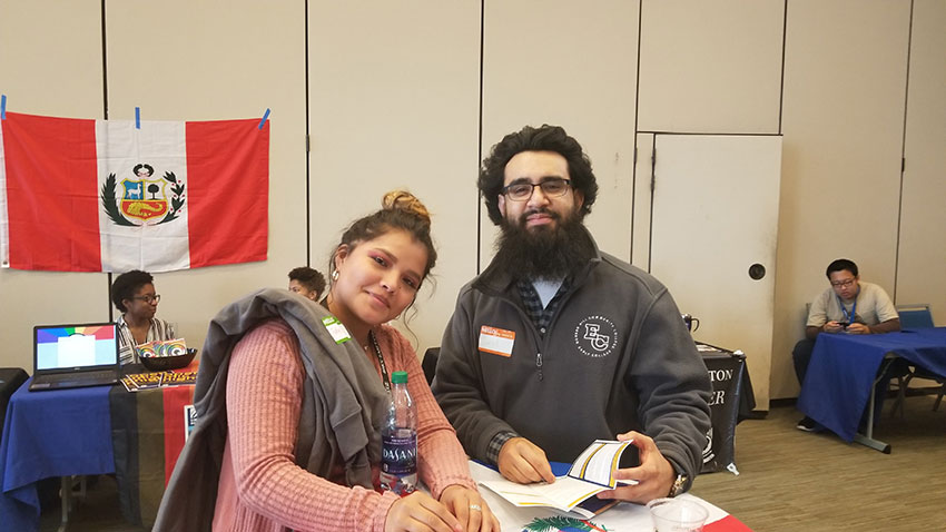 Two students smiling at the camera while writing.